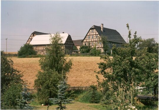 Blick über ein Feld zu einem Vierseitenhof in Lichtenstein