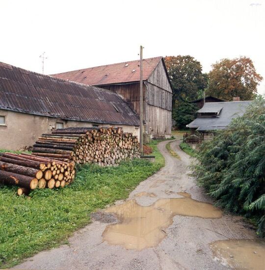 Einfahrt zu einem Bauernhof mit Holzstapeln in Stein