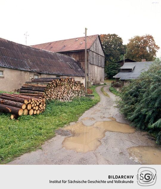 Einfahrt zu einem Bauernhof mit Holzstapeln in Stein