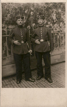 Postkarte: Zwei Soldaten aufgenommen vor einem Hintergrund mit Gartenmotiv