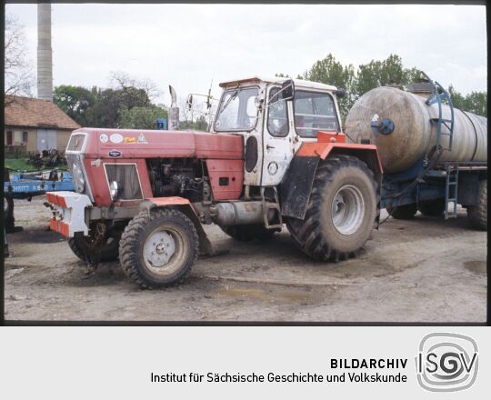 Traktor der LPG Großwelka mit einem Tankwagen. Der Traktor ist unter anderem mit aufklebern westlicher Unternehmen beklebt.