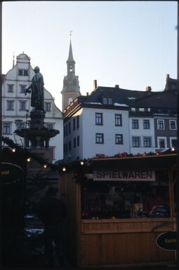 Bild: Verkaufsstand auf dem Freiberger Weihnachtsmarkt, im Hintergrund das Brunnendenkmal für Otto den Reichen und ein Turm der Petrikirche