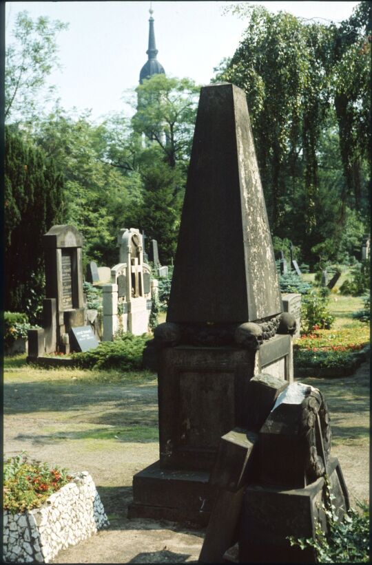 Grabstein in Form eines Obelisken auf dem Trinitatisfriedhof in der Dresdner Johannstadt, im Hintergrund der Kirchturm der Trinitatiskirche