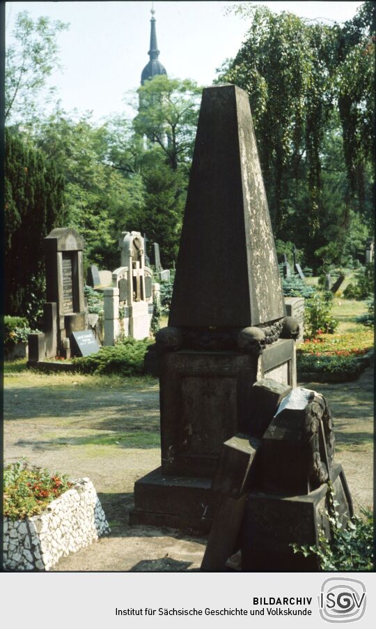Grabstein in Form eines Obelisken auf dem Trinitatisfriedhof in der Dresdner Johannstadt, im Hintergrund der Kirchturm der Trinitatiskirche