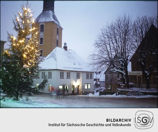 Verschneiter Marktplatz mit Weihnachtsbaum in Hohnstein in der Sächsischen Schweiz, im Hintergrund ist der Turm der Stadtkirche abgebildet