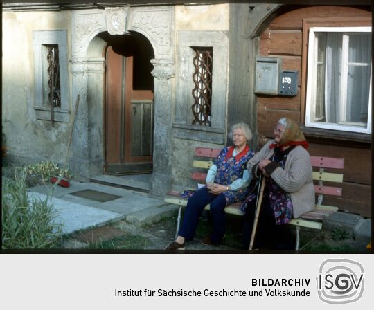 Zwei Frauen auf einer Bank vor einem Umgebindehaus mit Steinportal mit Rokokodekor in Waltersdorf 1994