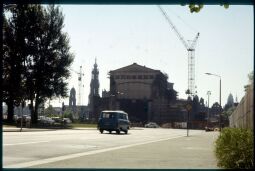 Bild: Blick auf die Westseite der Semperoper in Dresden während der Rekunstruktion und dem Bau der Erweiterungsbauten 1984. Im Hintergrund sind die Türme des Ständehauses, der Katholischen Hofkirche, des Schlosses und des Rathauses abgebildet.