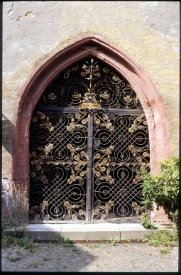Bild: Portal zur Vorhalle der Kirche St. Johannis in Mügeln 1995. Das Portal ist mit einerm aufwändigen Schmiedeisernen Gittern (datiert auf das Jahr 1648) verschlossen.