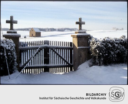 Blick durch das Friedhofstor in Kleinröhrsdorf auf verschneite Felder.