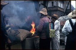 Bild: Umzug der Schifferfastnacht in Postelwitz 1959: Teilnehmer an einem Feuer, ein Teilnehmer hat verschiedene Verpackungen (Kaffe) an seinem Rücken befestigt