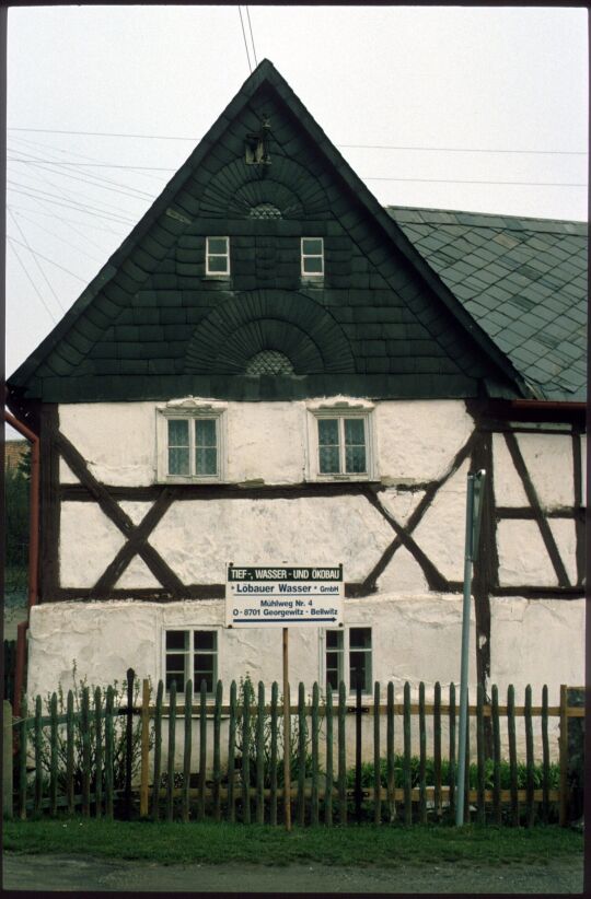 Werbeschild vor einem Fachwerkhaus mit verschiefertem Giebel