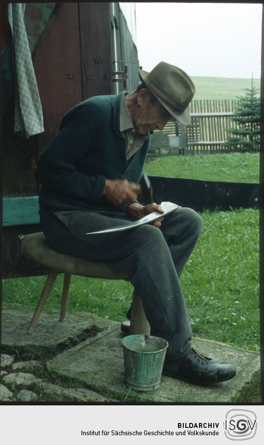 Bauer beim Dengel eines Sensenblatt in Marieney im Vogtland