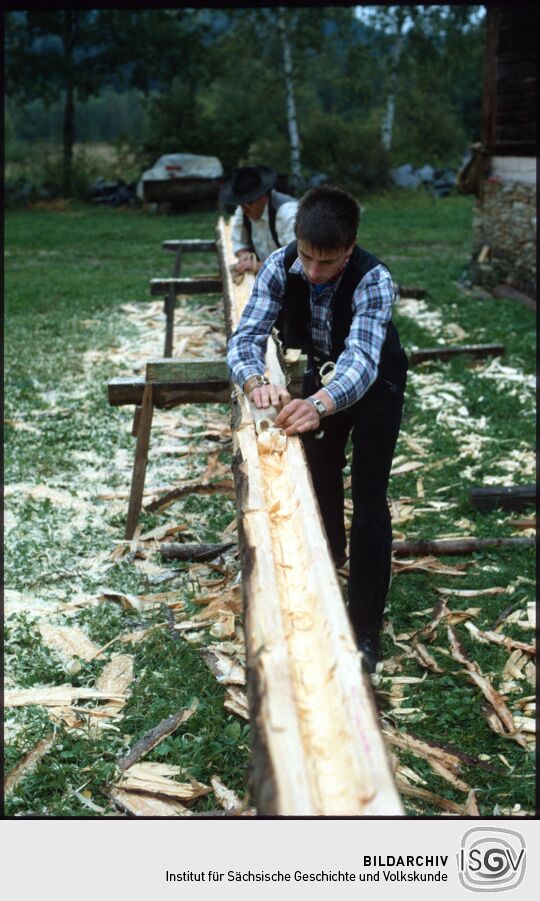Zimmerleute bei der Arbeit an einem Baumstamm in Landwüst