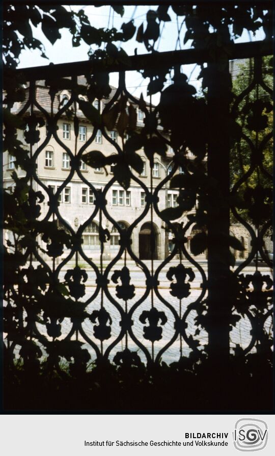 Blick durch ein Gitter des Eliasfriedhof zum Stadthaus Johannstasdt