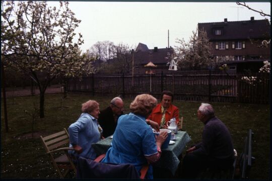 Fünf Personen an einer Kafeetafel in einem Garten