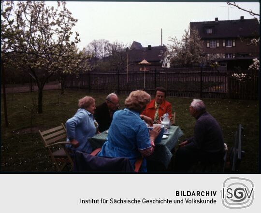 Fünf Personen an einer Kafeetafel in einem Garten