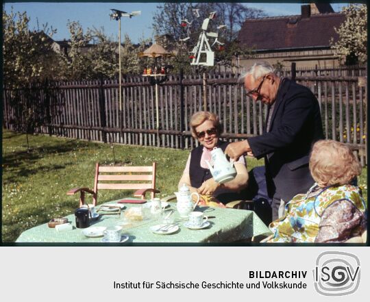 Drei ältere Personen an einer Kaffeetafel in einem Garten