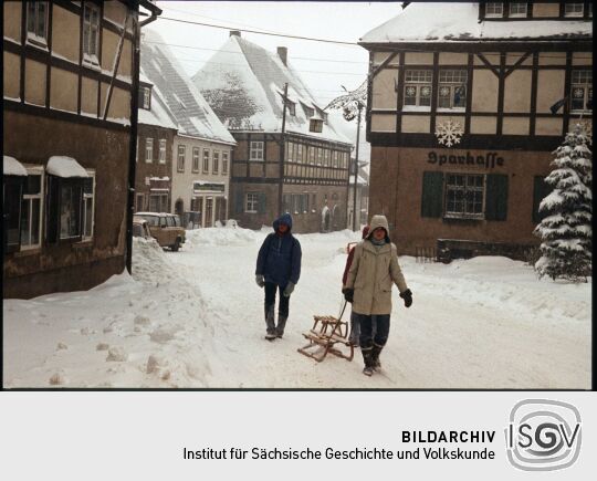 Drei Personen mit Schlitten vor dem verschneiten Rathaus Geising