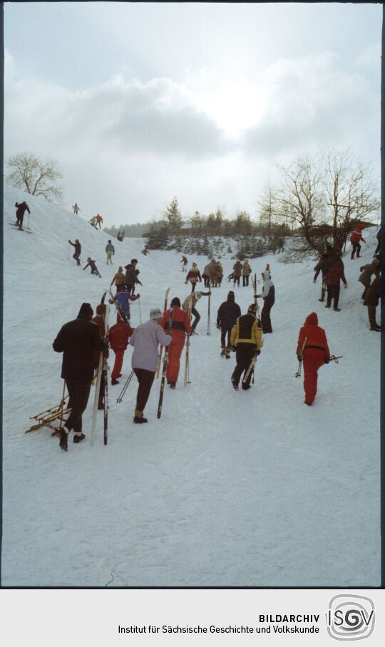 Wintersportler mit Skis und Schlitten an einem Hang in Geising
