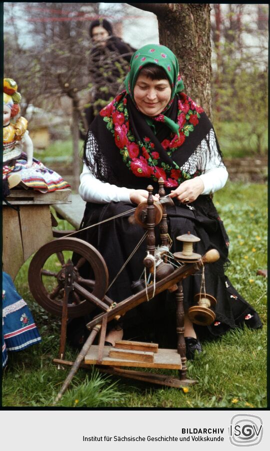 Frau in Tracht an einem Spinnrad in Leutersdorf