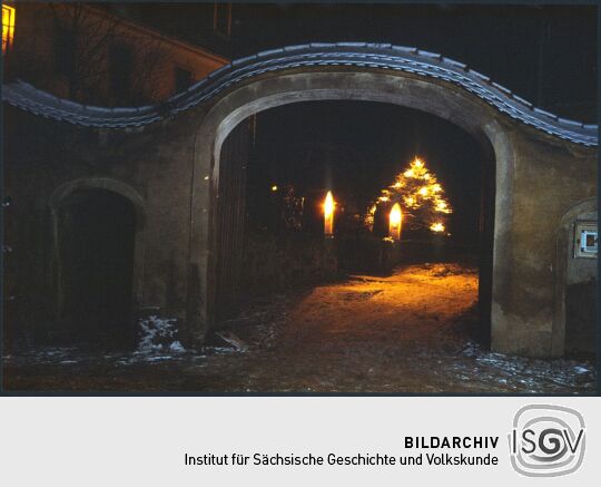 Blick durch das Tor des Pfarrhofs Wachau zu einem verschneiten Weihnachtsbaum