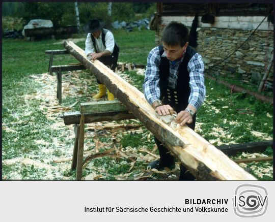 Zimmerleute beim Hobeln eines Baumstammes in Landwüst