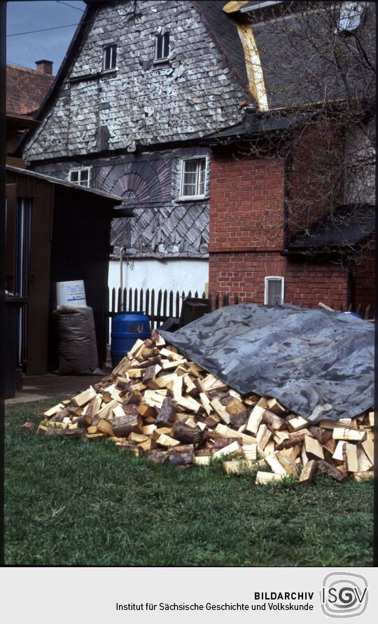 Brennholzhaufen vor einer verschieferten Fassade in Jonsdorf