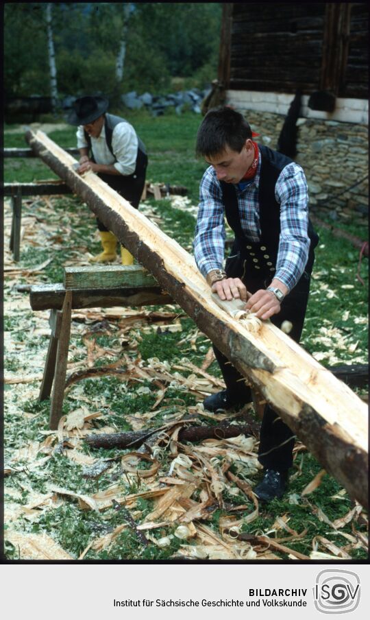 Zimmerleute beim Hobeln eines Baumstammes in Landwüst
