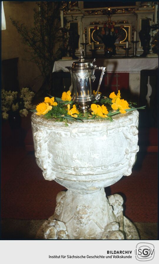 Eine Kanne auf dem blumengeschmückten Taufstein in der Kirche Schellerhau