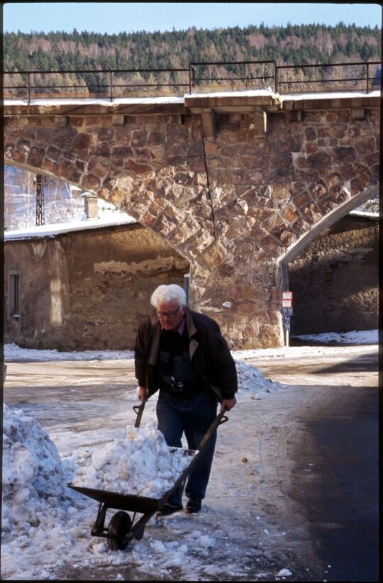 Mann beim Schneeschippen mit einer Schubkarre vor dem Eisenbahnviadukt in Schmiedeberg