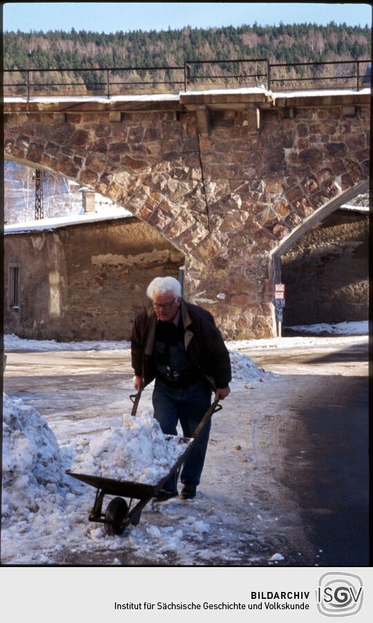 Mann beim Schneeschippen mit einer Schubkarre vor dem Eisenbahnviadukt in Schmiedeberg