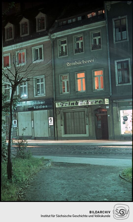 Zwei Gebäude in der Dresdner Heinrichstraße mit einem Optikergeschäft und deiner Feinebäckerei bei Nacht