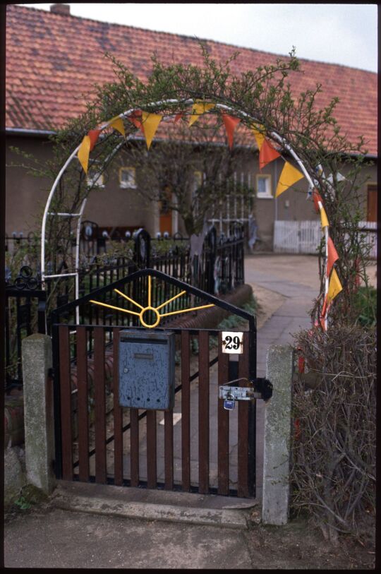 Eingangstor zu einem Hof mit einem wimpelgeschmückten Rosenbogen in Rosenhain