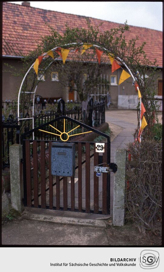 Eingangstor zu einem Hof mit einem wimpelgeschmückten Rosenbogen in Rosenhain
